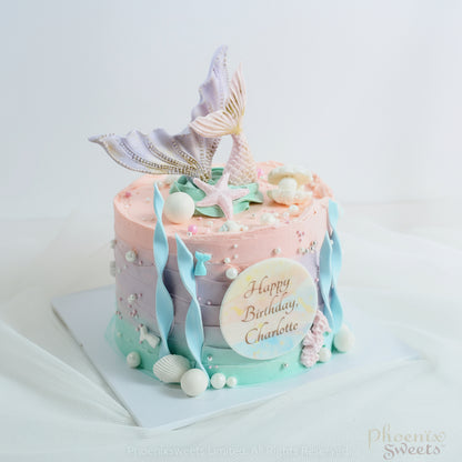 A beautifully decorated butter cream cake with mermaid tails, pearls, and a custom fondant plate reading 'Happy Birthday, Charlotte'.
